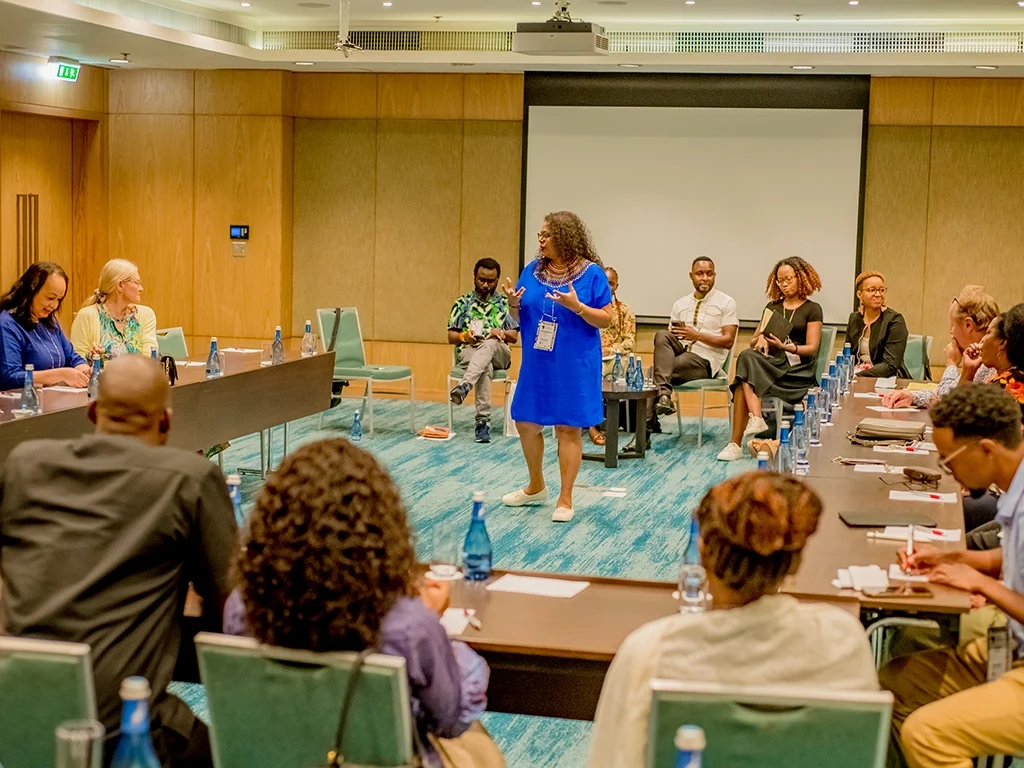 Facilitator in a blue dress leading an interactive theory-of-change workshop with ALI-East Africa fellows seated in a dialogue circle.